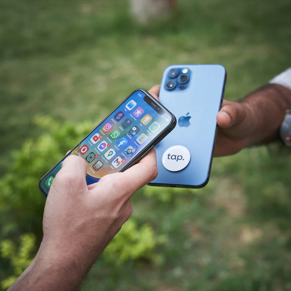 Person holding smartphone with icons visible parallel to another smartphone with white tap. NFC sticker for sharing contactless information, outdoors.