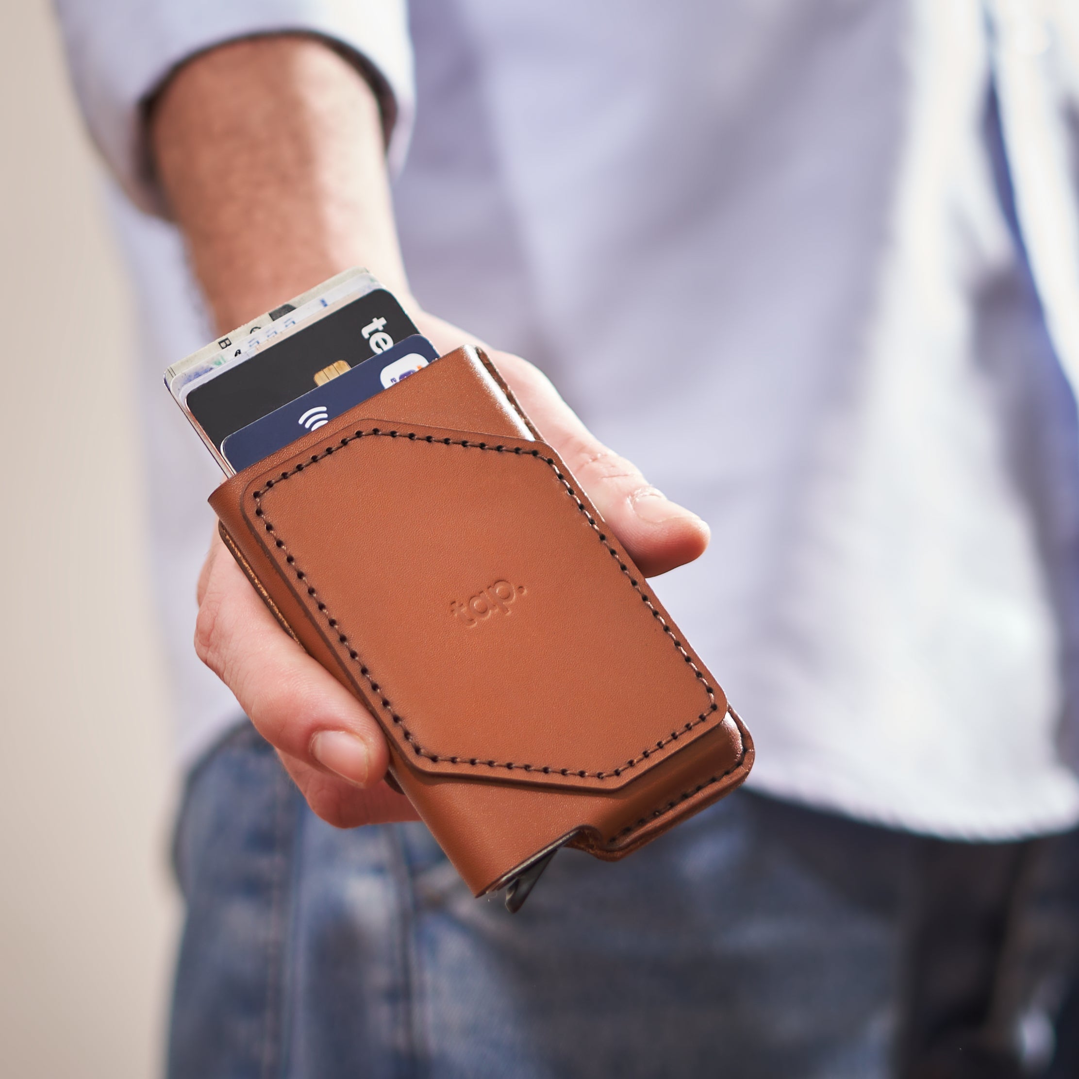 Man holding a Tap brown leather wallet case featuring card slots.