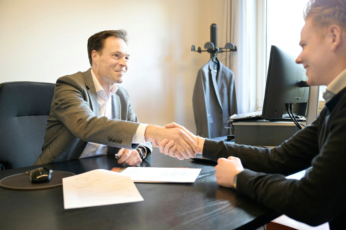 Two people shake hands across a desk after a meeting