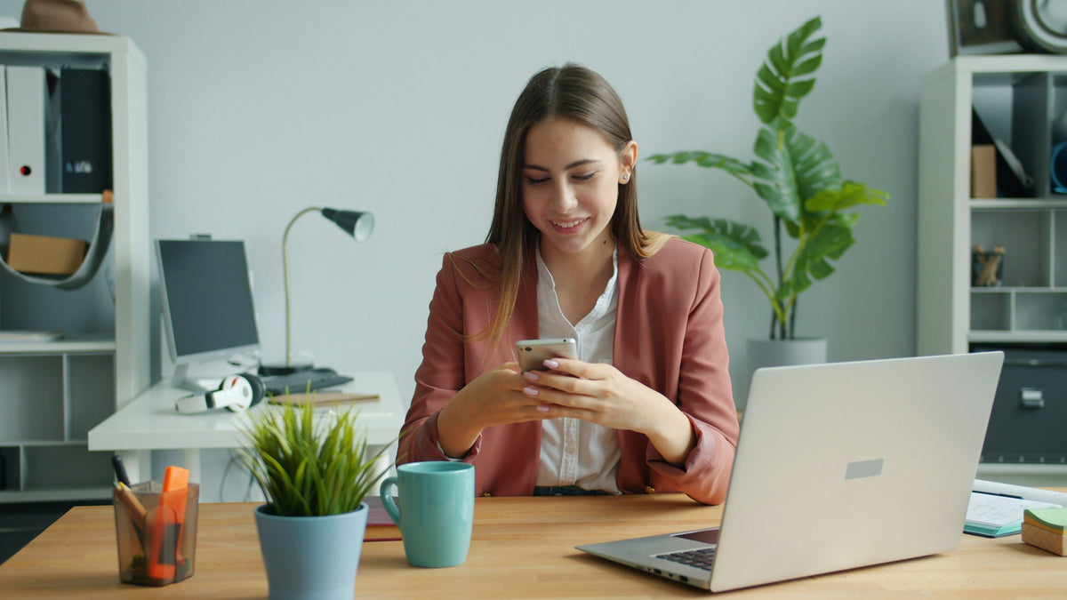 A woman checks her phone at her desk